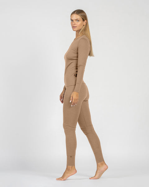 Kvinde iført en beige heldragt på hvid baggrund