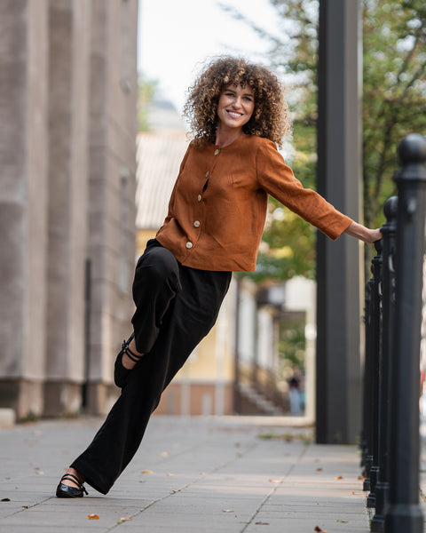 Kvinde med krøllet hår iført mandelbrun hørjakke Alice og stående på en gade