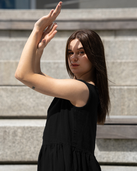 Woman wearing black linen sleeveless dress with relaxed fit and gathered waist detail, breathable lightweight summer linen dress styled in urban setting
