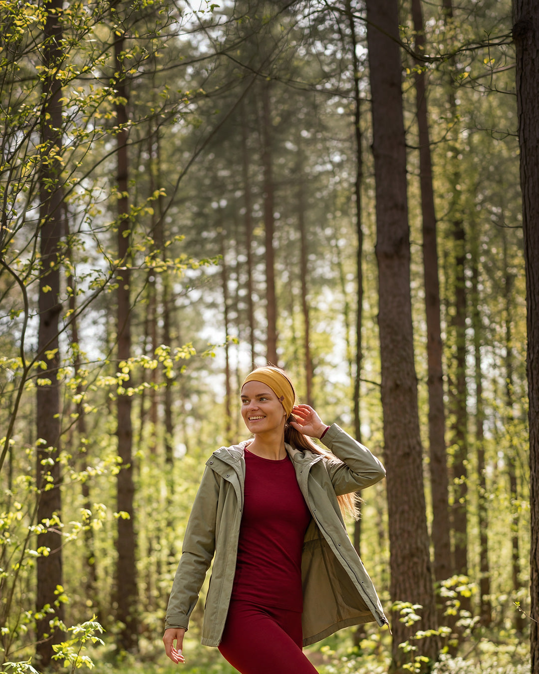 Woman walking in a forest wearing red merino wool base layer and outdoor jacket, breathable merino clothing for hiking and outdoor activities.