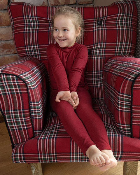 a girl sitting in a red checkered pattern armchair, wearing the menique Kids' Merino 160 Long Sleeve Crew in Royal Cherry Color.