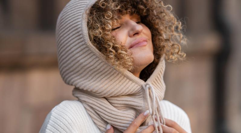 a woman with her eyes closed, wearing the menique knit balaclava hood in beige color.