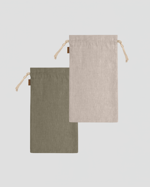 A studio laydown of two medium rectangular linen bread bags against a plain light gray background. One bag is olive green and the other is a natural beige color. Both feature natural rope drawstrings and small brown brand tags.