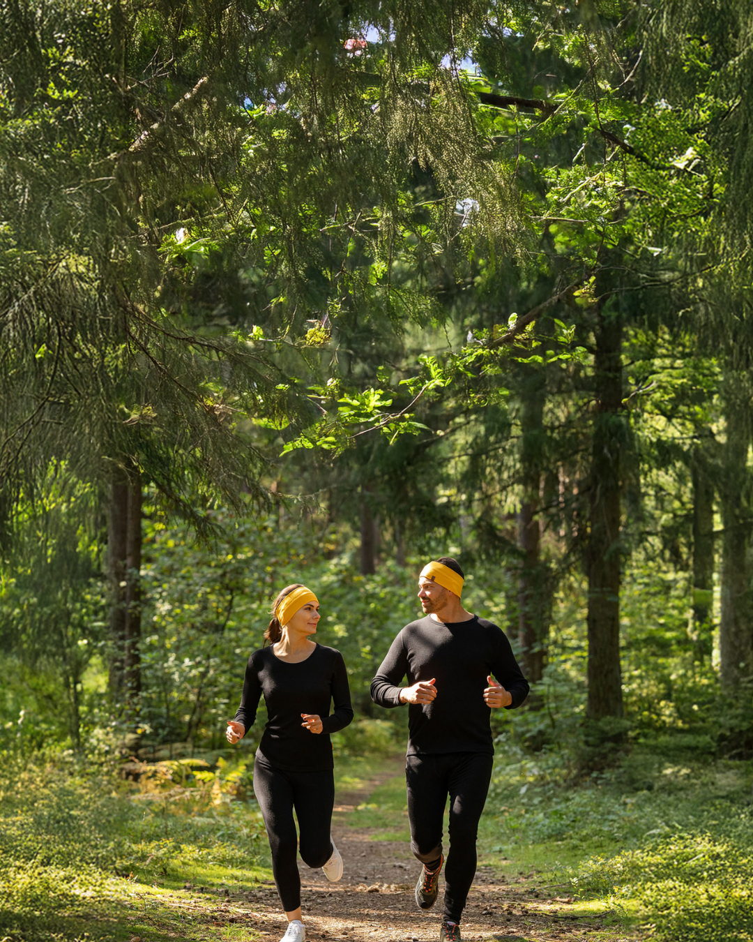Man and woman running in forest wearing merino wool activewear and headbands, breathable moisture-wicking clothing for outdoor sports.