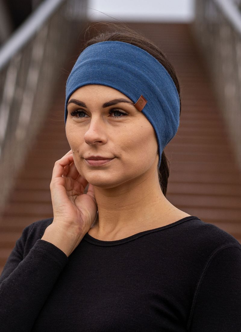Woman wearing a blue headband with a brand logo, standing outdoors.