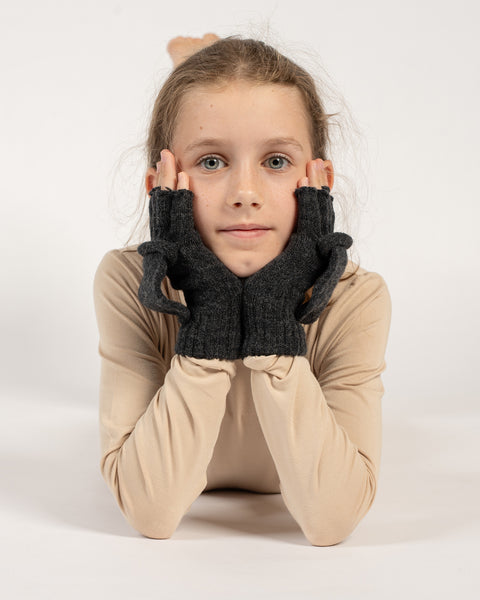 Pige liggende med hovedet hvilende på hænderne, iført mørkegrå strikkede konvertible vanter med åbne vanteklapper.