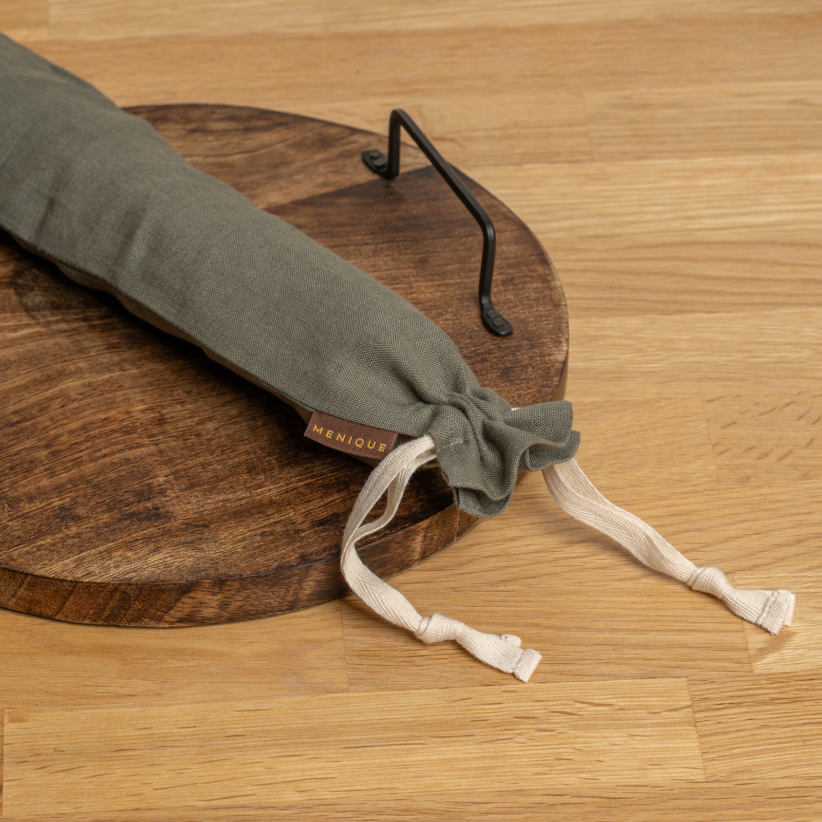 Lang brødpose hængende på en krog med brød og køkkenredskaber på et bord.