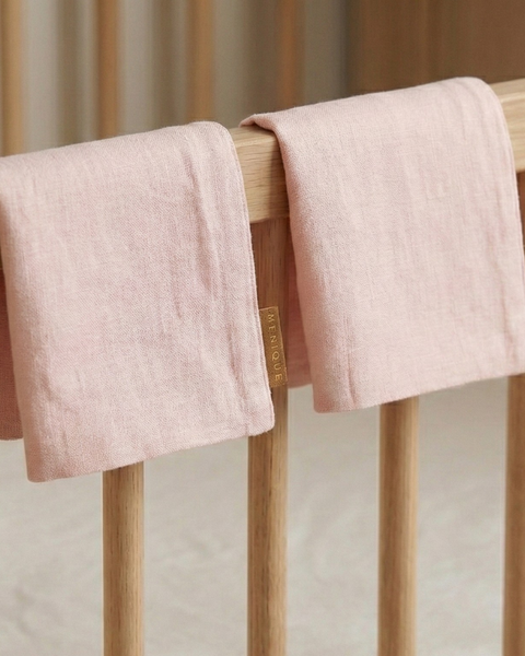 Dusty pink linen baby burp cloth hanging on wooden crib rail, breathable absorbent newborn burping and feeding essential