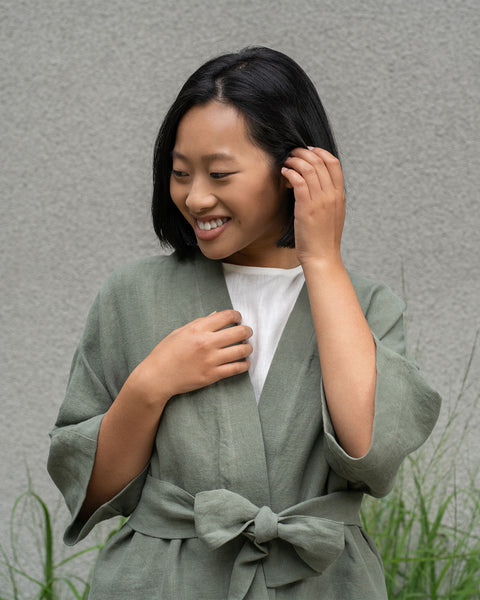 Kvinde med kort mørkt hår iført en stengrøn hørjakke og stengrønne menique bukser.