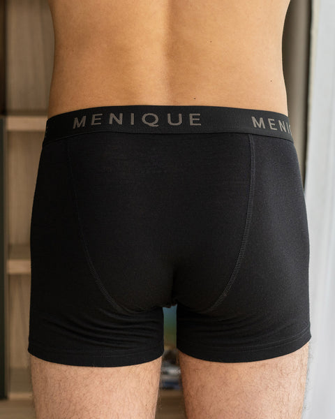 En mand iført korte boksershorts lavet af merinouldstof, i farven sort. Bagsiden af boksershortsene er synlig på billedet.