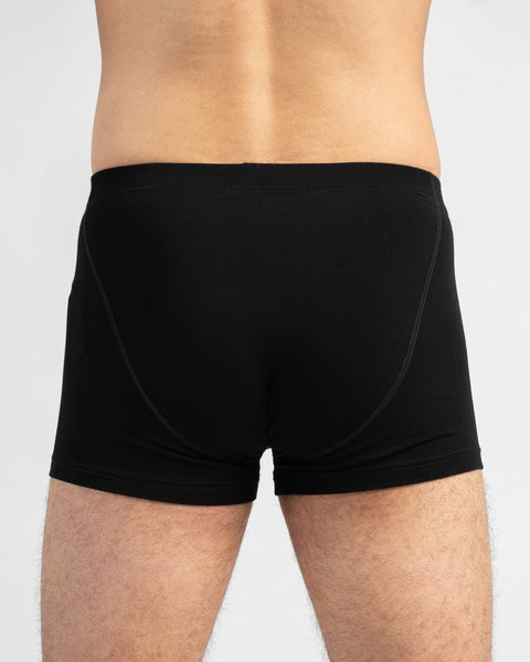 A close-up studio shot showing the back of a man wearing fitted black boxer briefs. The image highlights the rear seam details and contouring fit of the underwear.