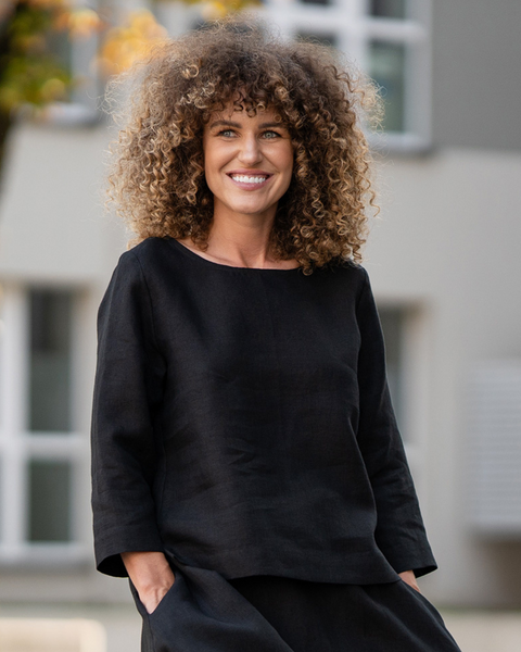 Kvinde iført en sort hørbluse stående udendørs med sløret baggrund