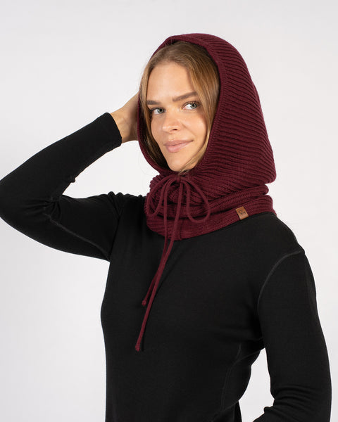 Woman wearing a royal cherry knitted merino wool hood balaclava with drawstrings, hand touching head.