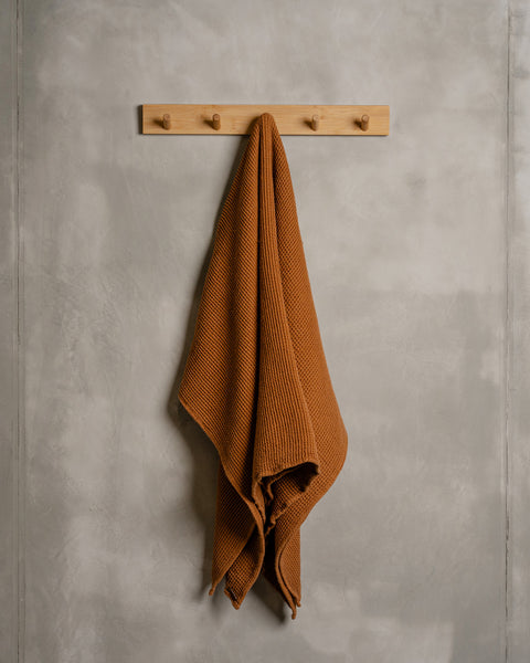 A linen &amp; cotton waffle body towel in almond brown color hanging on a wooden rack.