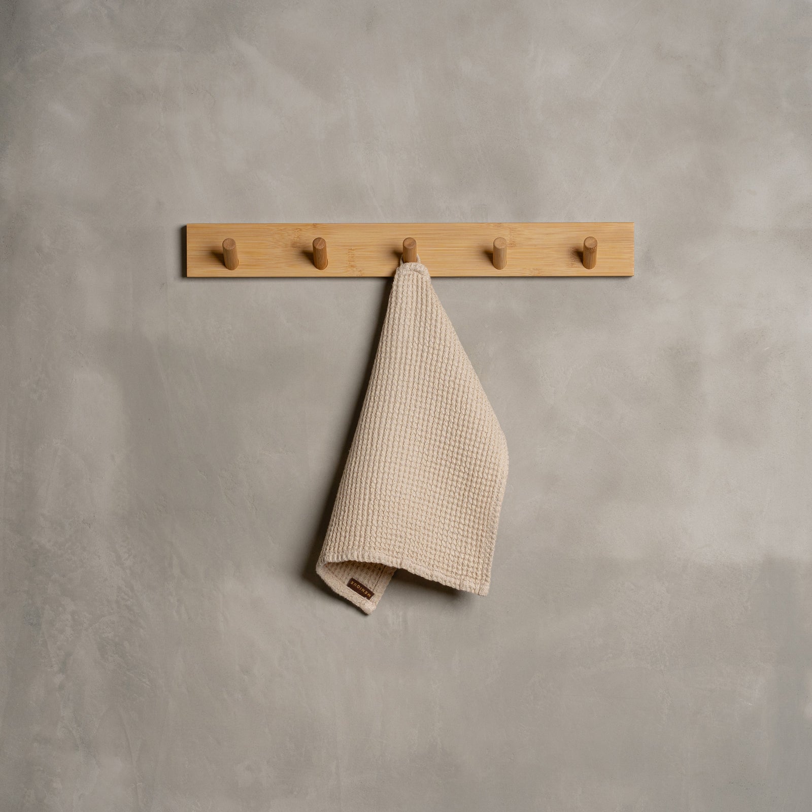 En kvinde holder et vaffelvaskeklud ansigtshåndklæde på 30x30 cm ved sit ansigt, i farven Sandbrun.