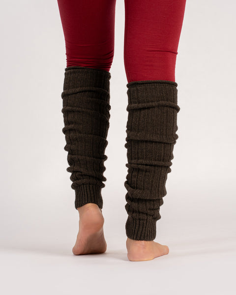 Set bagfra af en person, der står barfodet iført brune, ribstrikkede benvarmere, der er skubbet ned over røde leggings mod en ensfarvet lys grå baggrund.