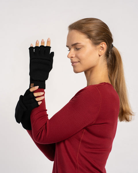 Halvnær billede af en kvinde i en rød bluse, med armene over kors og viser sorte ombyttelige vanter med klappen trukket tilbage, så fingrene kan ses.