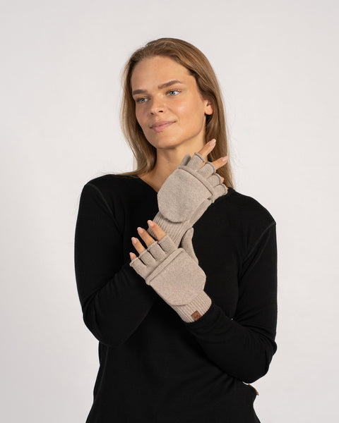 Trekvartbillede af modellen, der trækker en cremet-beige vendbar vante på med klappen foldet ind, armene let løftet.