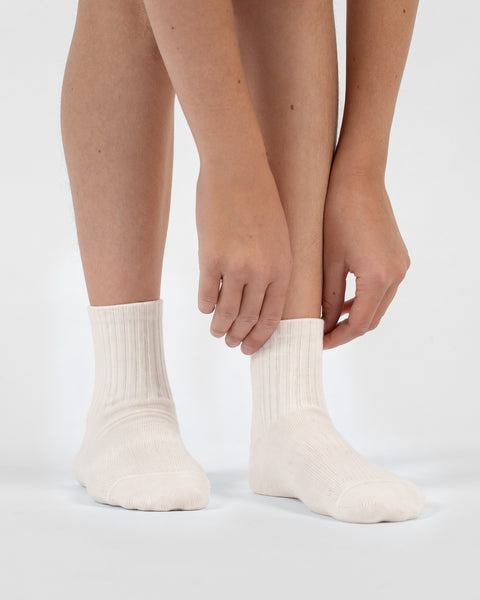 A person leaning down and using their hands to adjust the ribbed cuffs of their natural off-white crew socks.