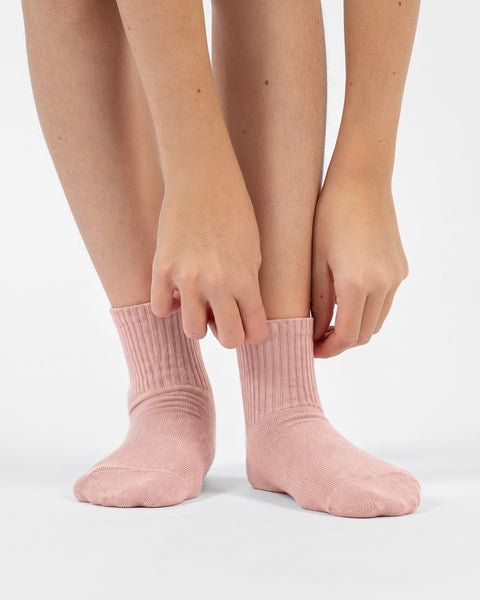 A person leaning down and using their hands to adjust the ribbed cuffs of their light pink crew socks.