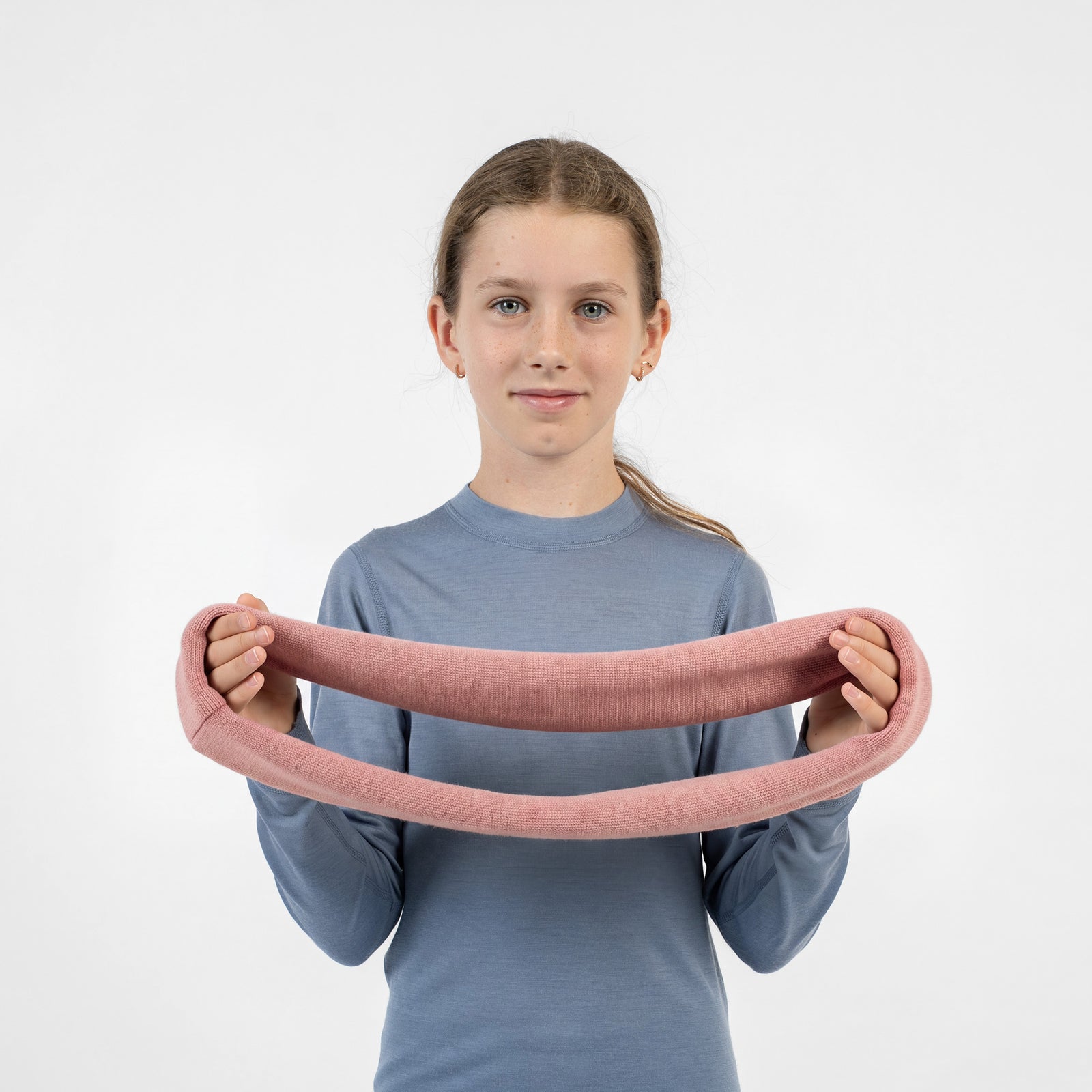 A young girl looking directly forward, wearing a beige knit infinity scarf around her neck and a blue long-sleeved shirt.