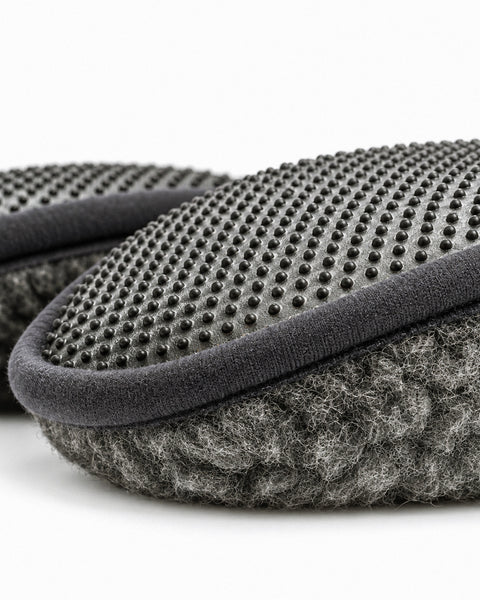 A close-up view of the bottom sole of a dark gray fuzzy slipper, highlighting an anti-slip design made of numerous small black rubber dots.