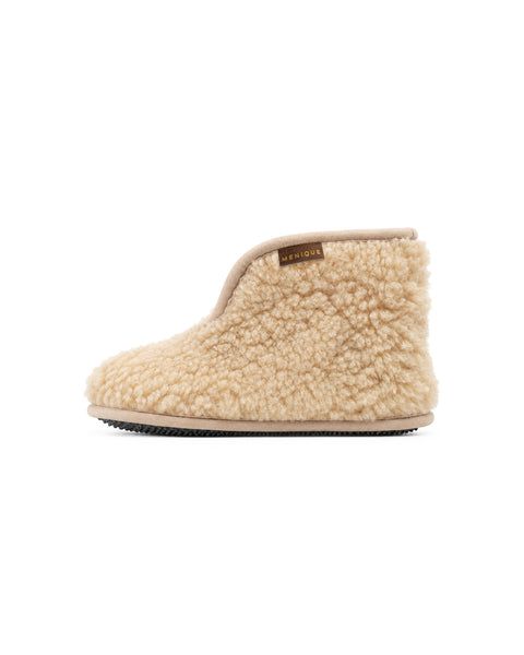 A side view of a single beige fuzzy ankle bootie slipper featuring a flat black sole, beige piping around the ankle opening, and a "MENIQUE" tag near the collar.