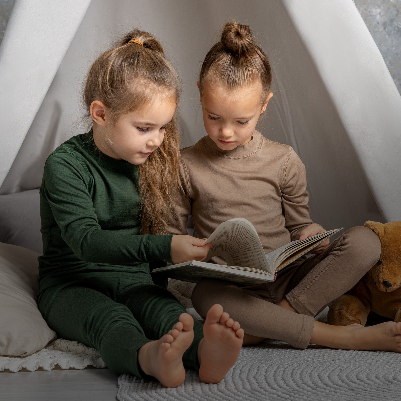 To børn sidder inde i et tipi og læser en bog.